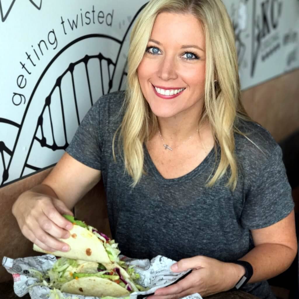 A blonde holding a taco and smiling