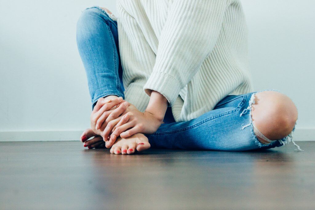 Woman in jeans and a white sweater who is barefoot