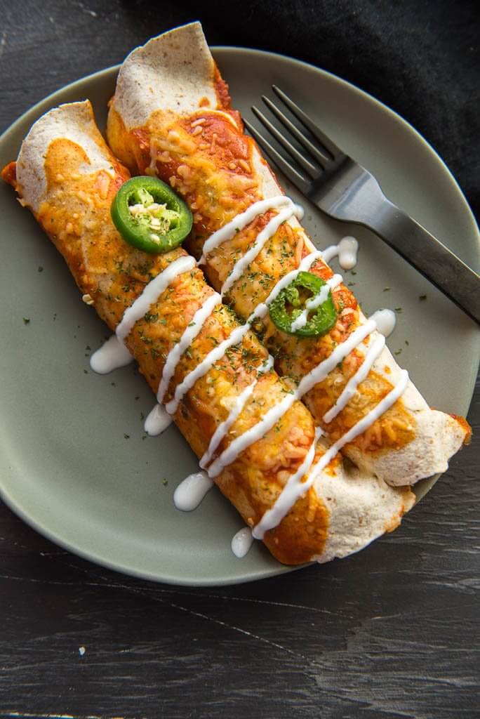 Overhead photo of two vegetarian enchiladas with drizzle and jalapeños