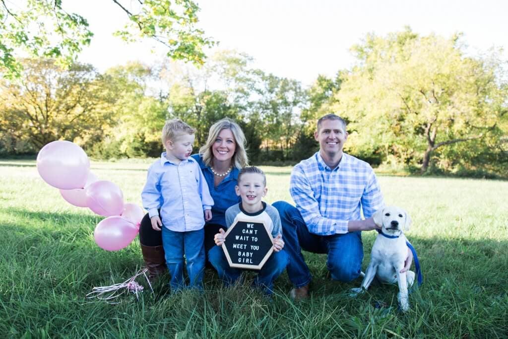 A woman, man and their 2 sons and dog holding pink balloons because they are going to have a little girl