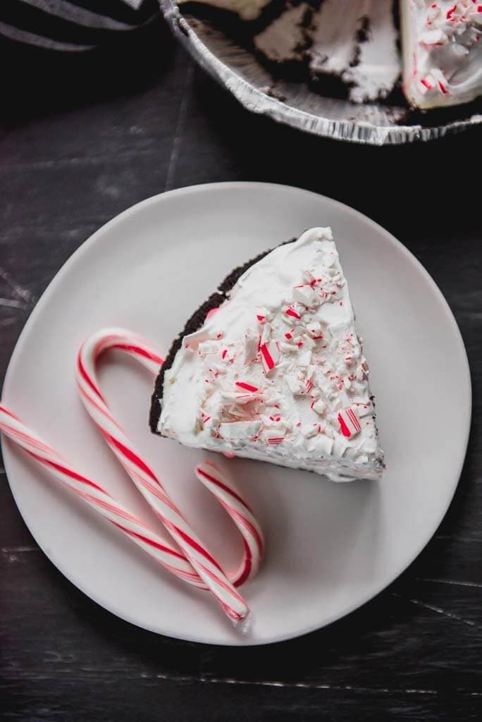 One slice of oreo pie with 2 candy canes on a white plate.