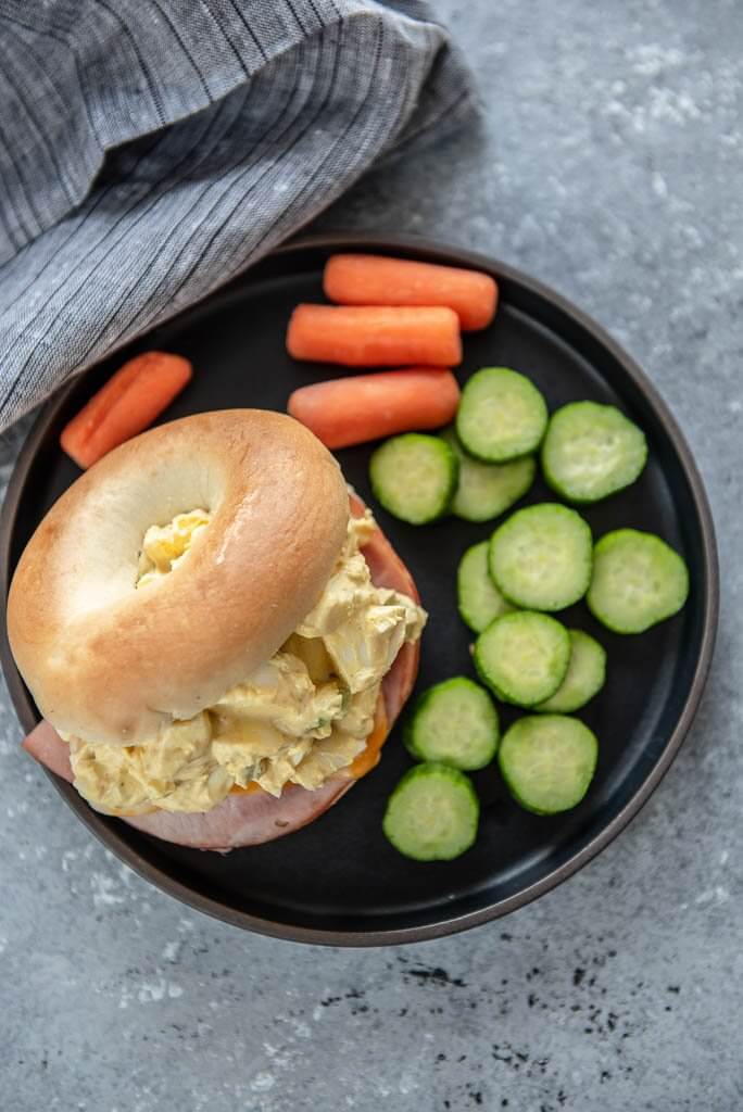 Overhead view of air fryer ham and cheese with egg salad on a black plate with vegetables
