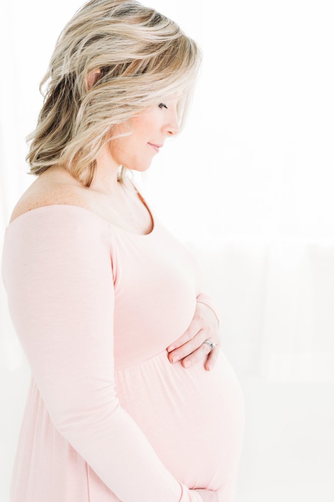 A woman in a pink dress who is pregnant looking at her belly for maternity photos