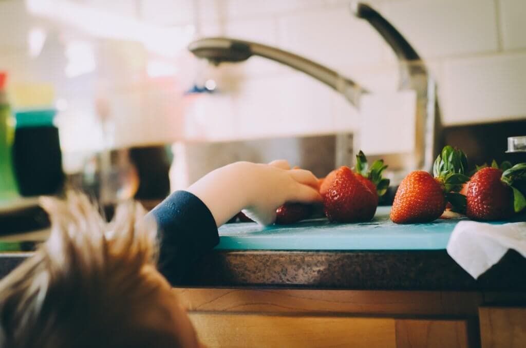  A little boy reaching for strawberries on a kitchen counter