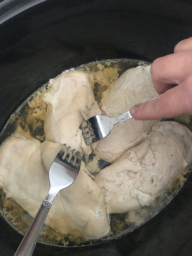 A woman shredding chicken with 2 forks in a slow cooker