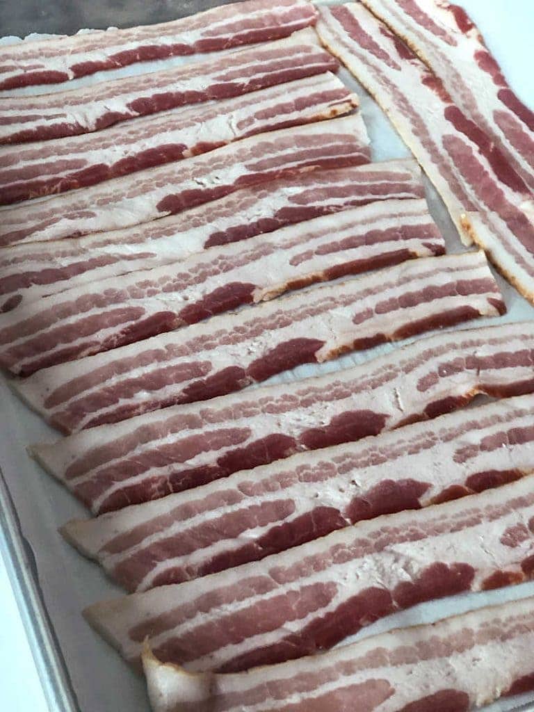 Raw bacon lined out on a rimmed baking sheet
