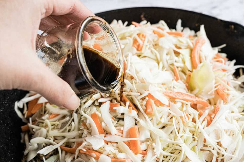A woman drizzling sauce over coleslaw in skillet