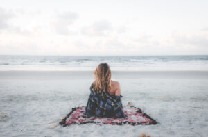a woman sitting on a blanket looking out at the beach