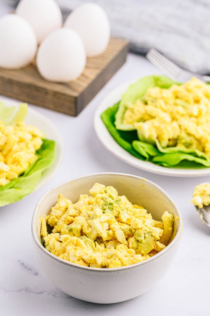 a bowl of avocado egg salad with a tray of eggs on a wooden holder