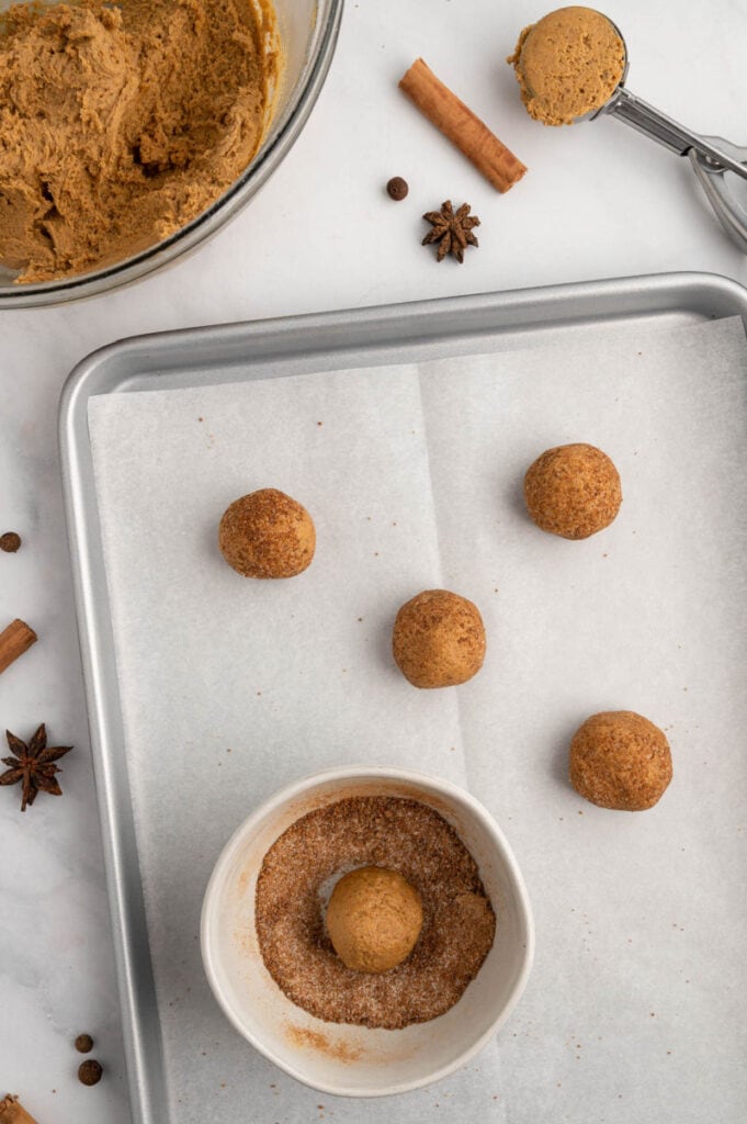 raw cookie dough on a cookie sheet with a bowl of spices to roll it into