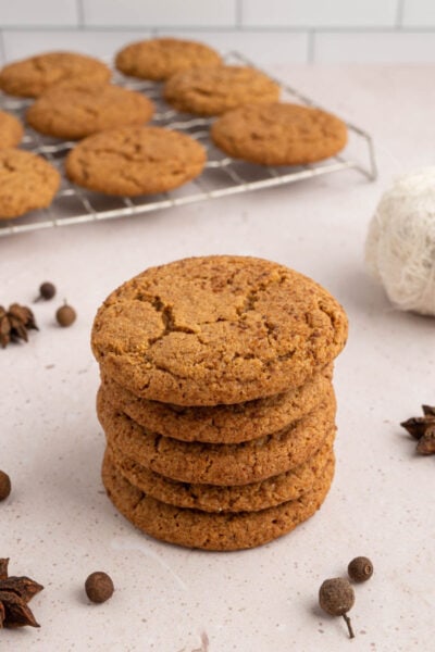 a stack of gluten free pumpkin cookies on a white background with cookies on a cookie sheet behind it